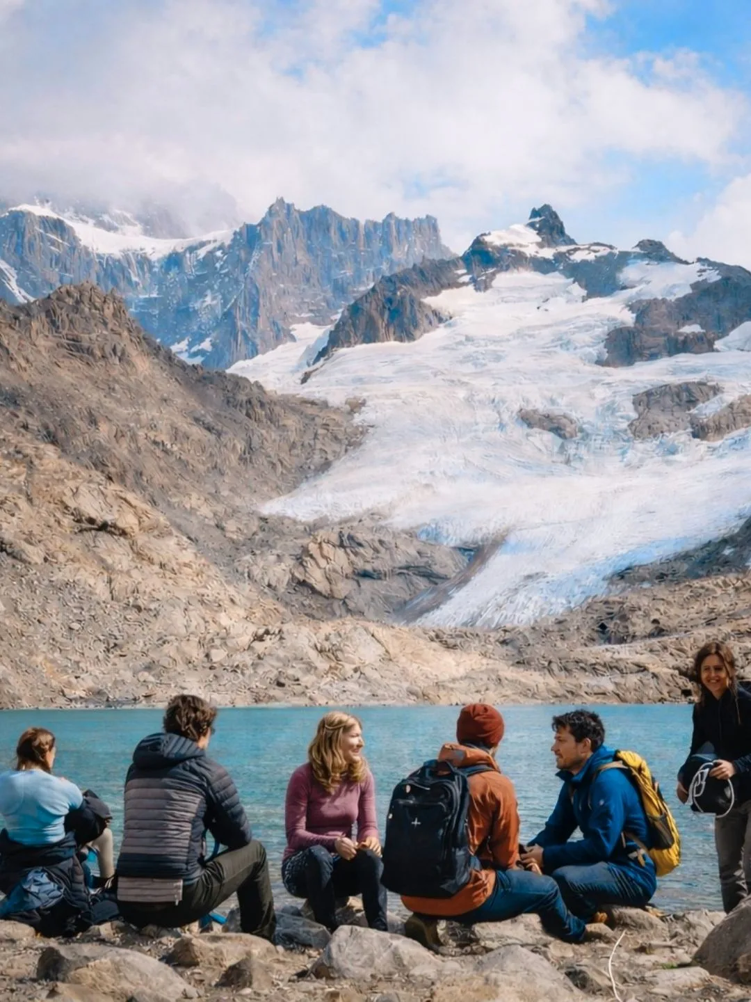 Un piccolo gruppo di viaggiatori seduto sulle rocce davanti a un ghiacciaio di montagna